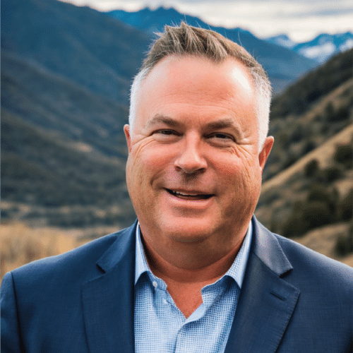 Jay smiling wearing a blue suit standing outdoors in a mountainous valley.