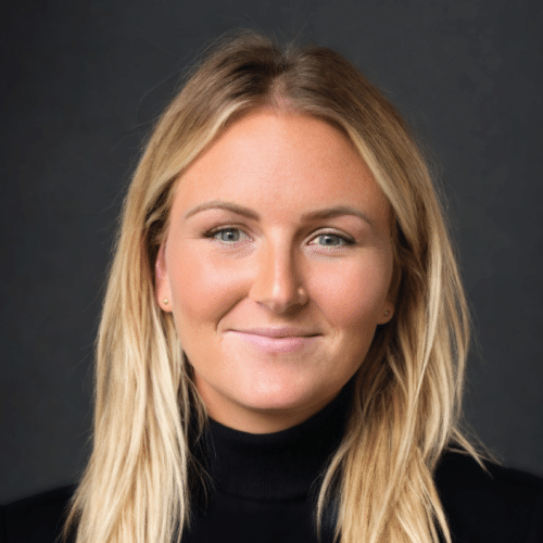 Jen smiling wearing a black turtleneck sweater standing in front of a dark grey background.