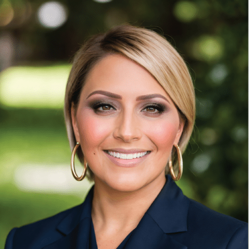 Joclynn smiling wearing a dark blue blazer standing in front of a green background.