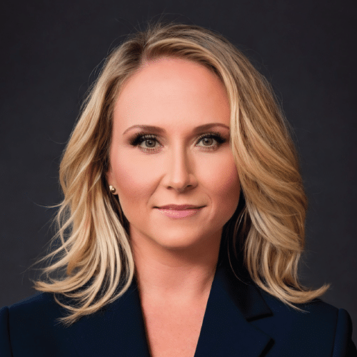 Karen smiling wearing a dark blue blazer standing in front of a grey background.