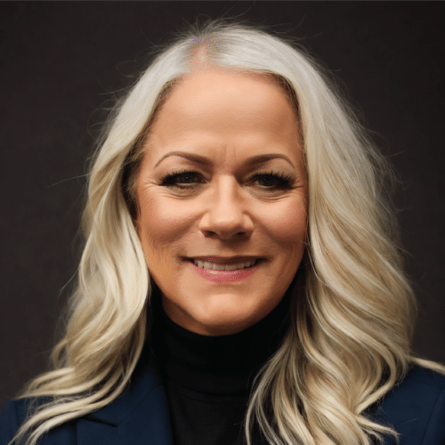 Lisa smiling wearing a dark blue blazer standing in front of a dark grey background.