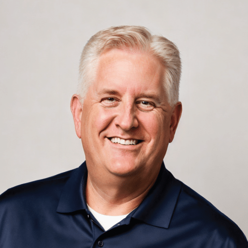 Scott smiling wearing a dark blue collared shirt with a light grey background.